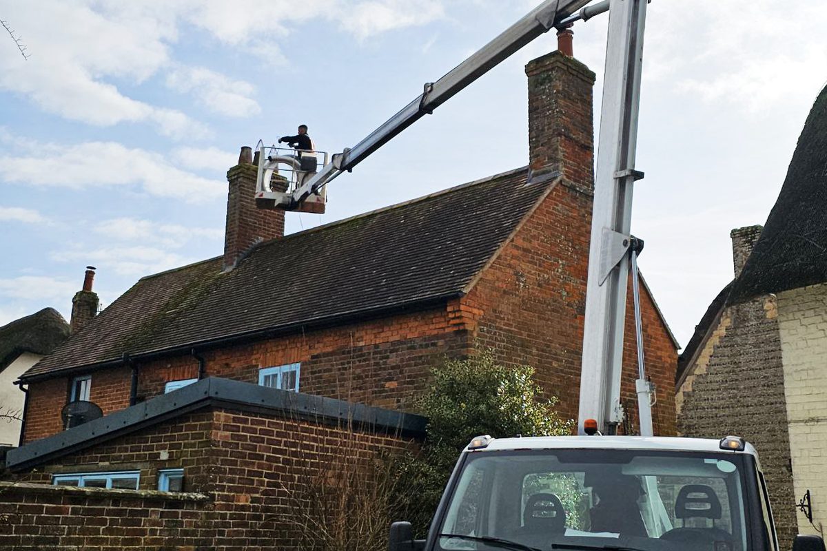 Operator working on a cottage chimney from the basket of a truck-mounted cherry picker