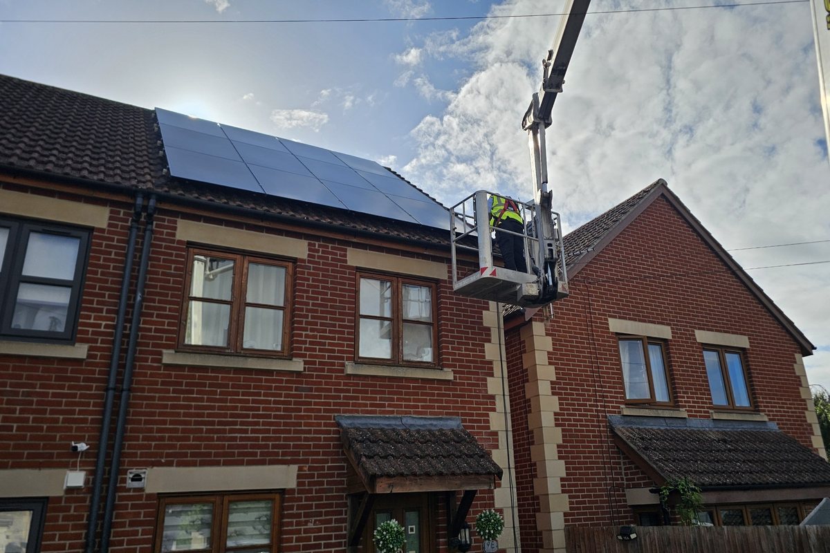 Operator in a cherry picker basket reaching roof-mounted solar panels on a house, working safely from the platform rather than from the roof