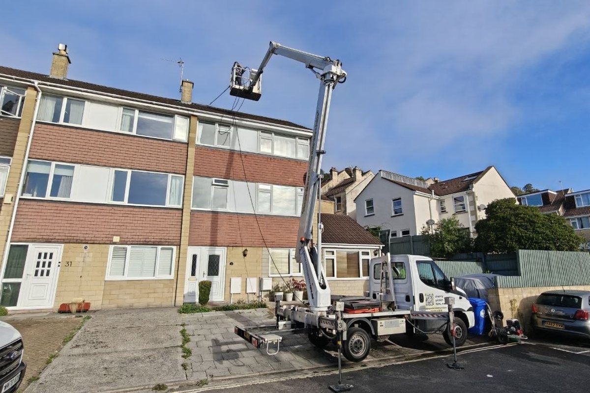 Truck-mounted cherry picker on outriggers in front of a three-storey terraced house in Bath, operator working at roof level
